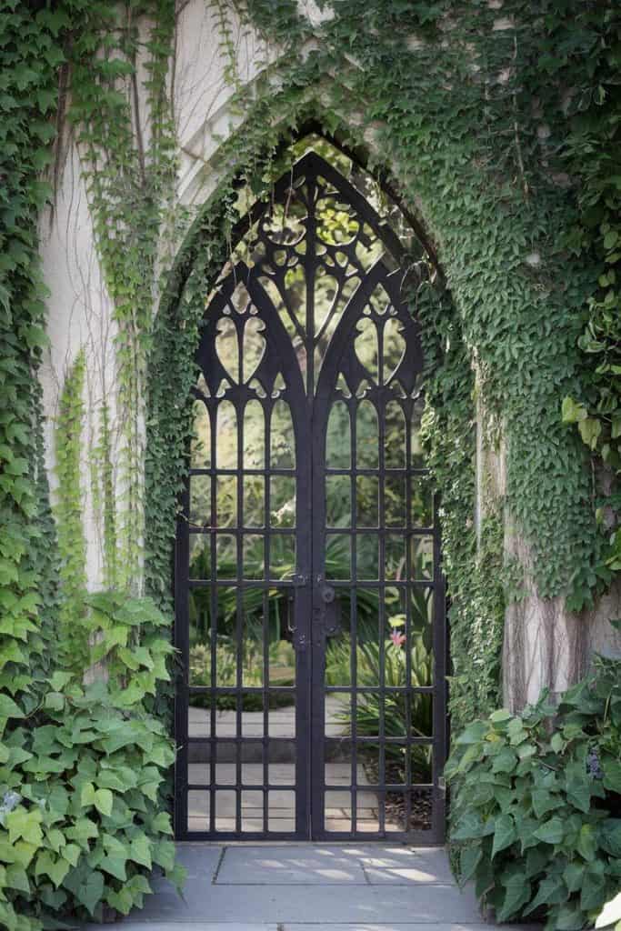 Gothic-style wrought iron gate surrounded by lush green ivy-covered walls.