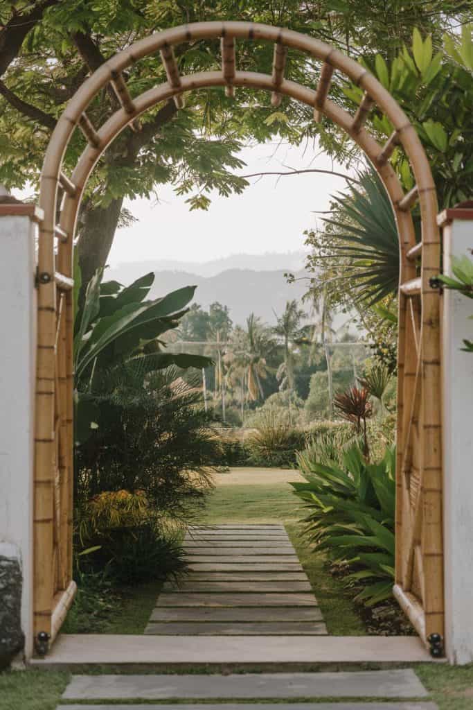 A bamboo arch frames a garden pathway lined with lush vegetation, leading to a view of distant mountains under a clear sky.