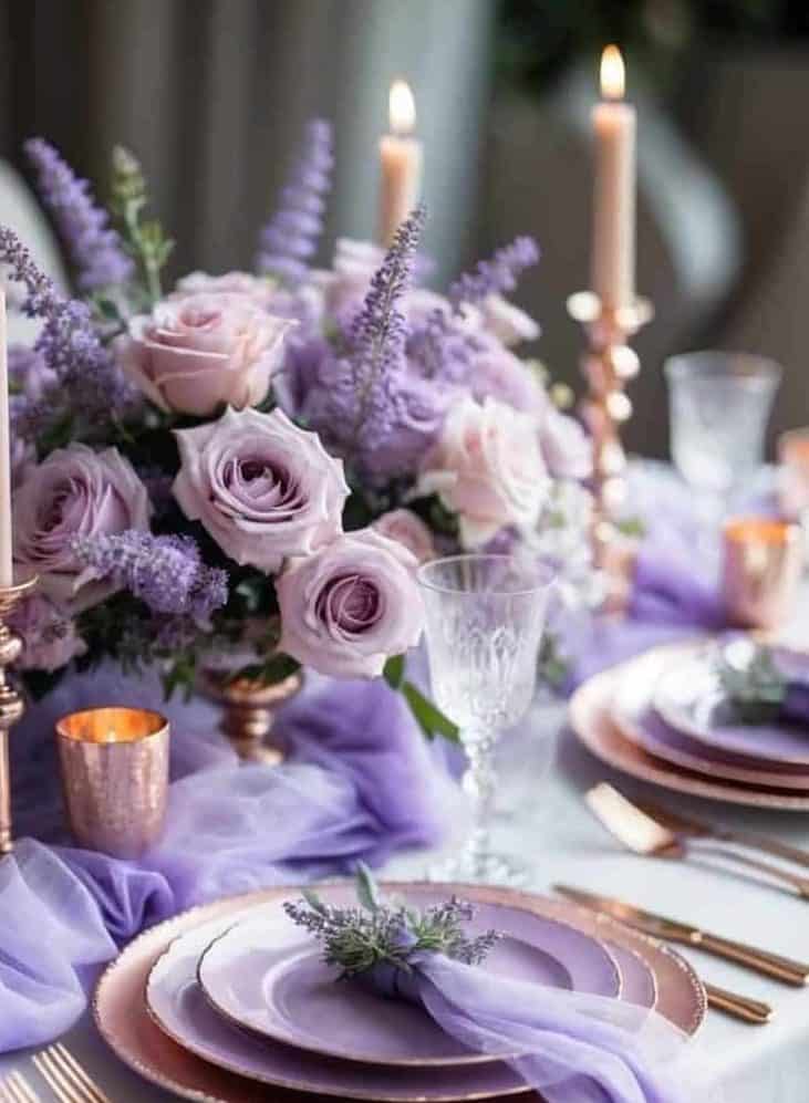 Elegant table setting with rose gold cutlery and plates, lavender napkins, lit candles, and a centerpiece of pink and purple flowers.