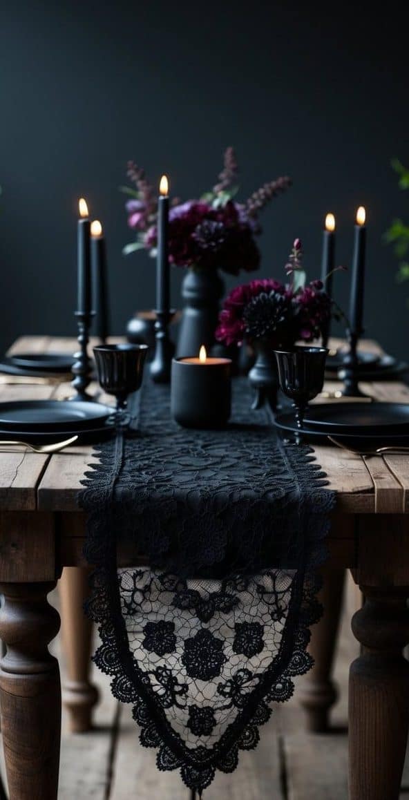 A wooden dining table set with black plates, black lace table runner, black candles, and dark floral arrangements against a dark background.