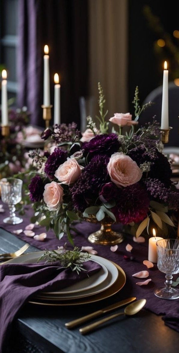Elegant dining table set with purple and pink floral arrangements, gold candlesticks with lit candles, and neatly arranged plates and cutlery.