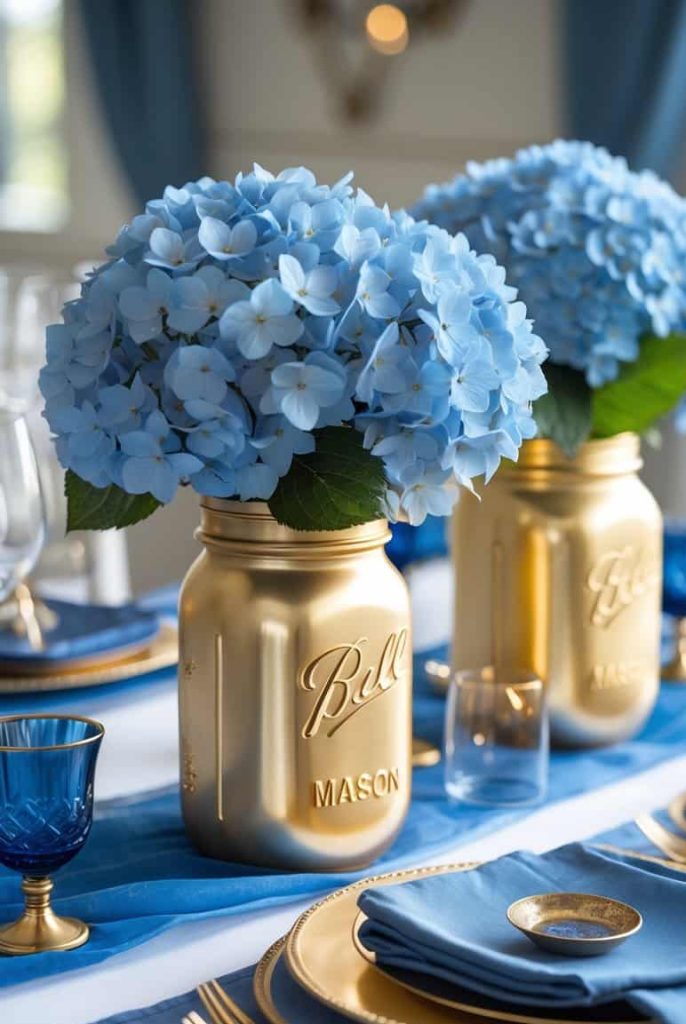 Two gold Mason jars filled with blue hydrangeas serve as centerpieces on a formal table set with blue napkins, blue glasses, and gold-rimmed plates.