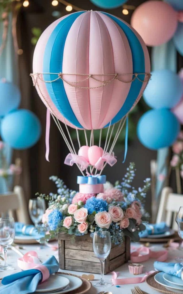 A table centerpiece features a pink and blue hot air balloon decoration above a box of roses and hydrangeas, surrounded by tableware and pastel balloons.
