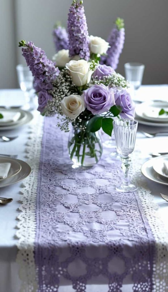 A table set for four with white plates, glasses, and silverware, featuring a vase of purple and white flowers on a lace and lavender table runner.