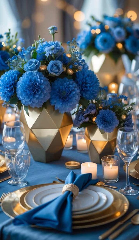 A formal table setting with gold-rimmed plates, blue napkins, glassware, candles, and gold vases filled with blue flowers. Warm string lights hang in the background.