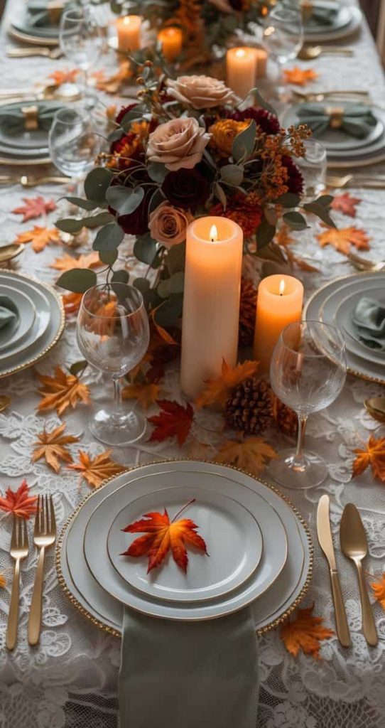 A formal dining table set with white and gold plates, gold cutlery, candles, autumn leaves, and floral centerpieces on a lace tablecloth.