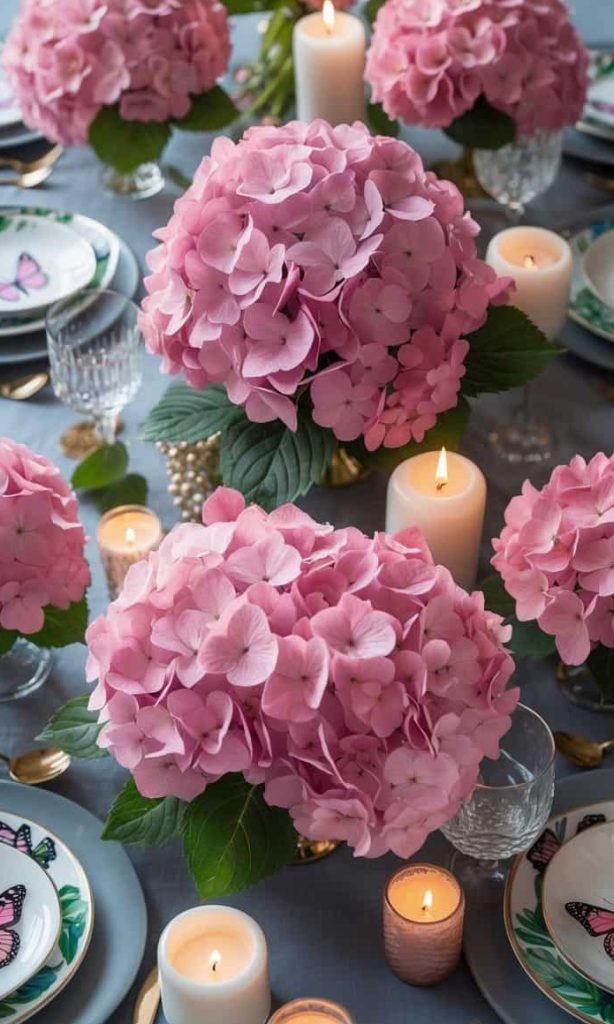 A dining table is set with pink hydrangea centerpieces, lit candles, crystal glassware, and plates decorated with butterfly designs.